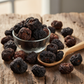 Black Chebulic Myrobalan (Haritaki Siyah/Kala Harar/Terminalia Chebula) dried dark black-brown wrinkled fruits on wooden surface with glass bowl and wooden spoon