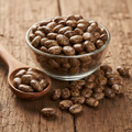 Castor Bean (Arind/Arand/Ricinus Communis) shiny mottled brown and cream seeds on wooden surface with glass bowl and wooden spoon