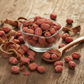 Ceylon Cornel (Peela Chandan/Cornus Capitata) dried reddish-pink fruits and bark pieces on wooden surface with glass bowl and wooden spoon