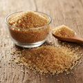Brown Sugar (Shakar/Saccharum Officinarum) golden-brown raw cane sugar crystals on wooden surface with glass bowl and wooden spoon
