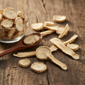 China Root (Chob Chini/Smilax China) dried pale cream and tan knobbly rhizome chips and slices on wooden surface with glass bowl and wooden spoon