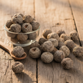 Beleric fruits (Bahera/Terminalia Bellirica) dried round grey-brown fruits on wooden surface with glass bowl and wooden spoon