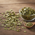 Centella (Brahmi/Gotu Kola/Centella Asiatica) dried small round fan-shaped green leaves on wooden surface with glass bowl and wooden spoon