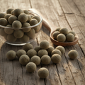 Bonduc Nut (Karanjwa/Caesalpinia Bonduc) hard grey-green round seeds on wooden surface with glass bowl and wooden spoon