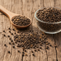 Babchi seeds (Bakuchi/Psoralea) on wooden surface with glass bowl and wooden spoon
